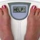 A scale that shows a weight loss plateau, person asking for help with strategies from a weight loss clinic near me to continue their weight loss goals.